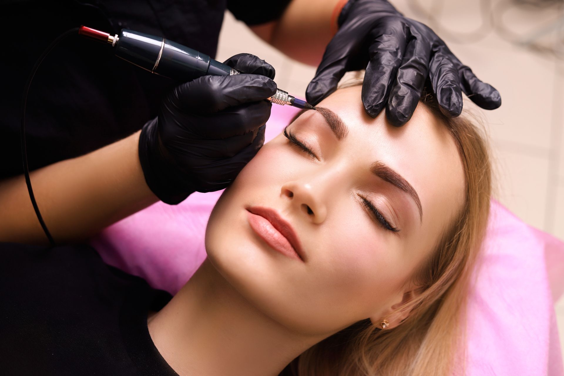 Aesthetic facial procedure with a gloved technician applying a treatment pen to a client’s forehead