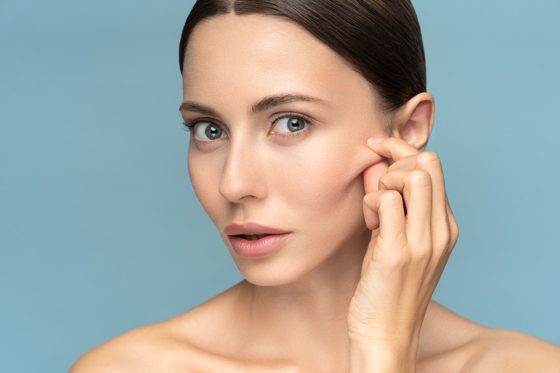 a woman is touching her face with her hand and looking at the camera .