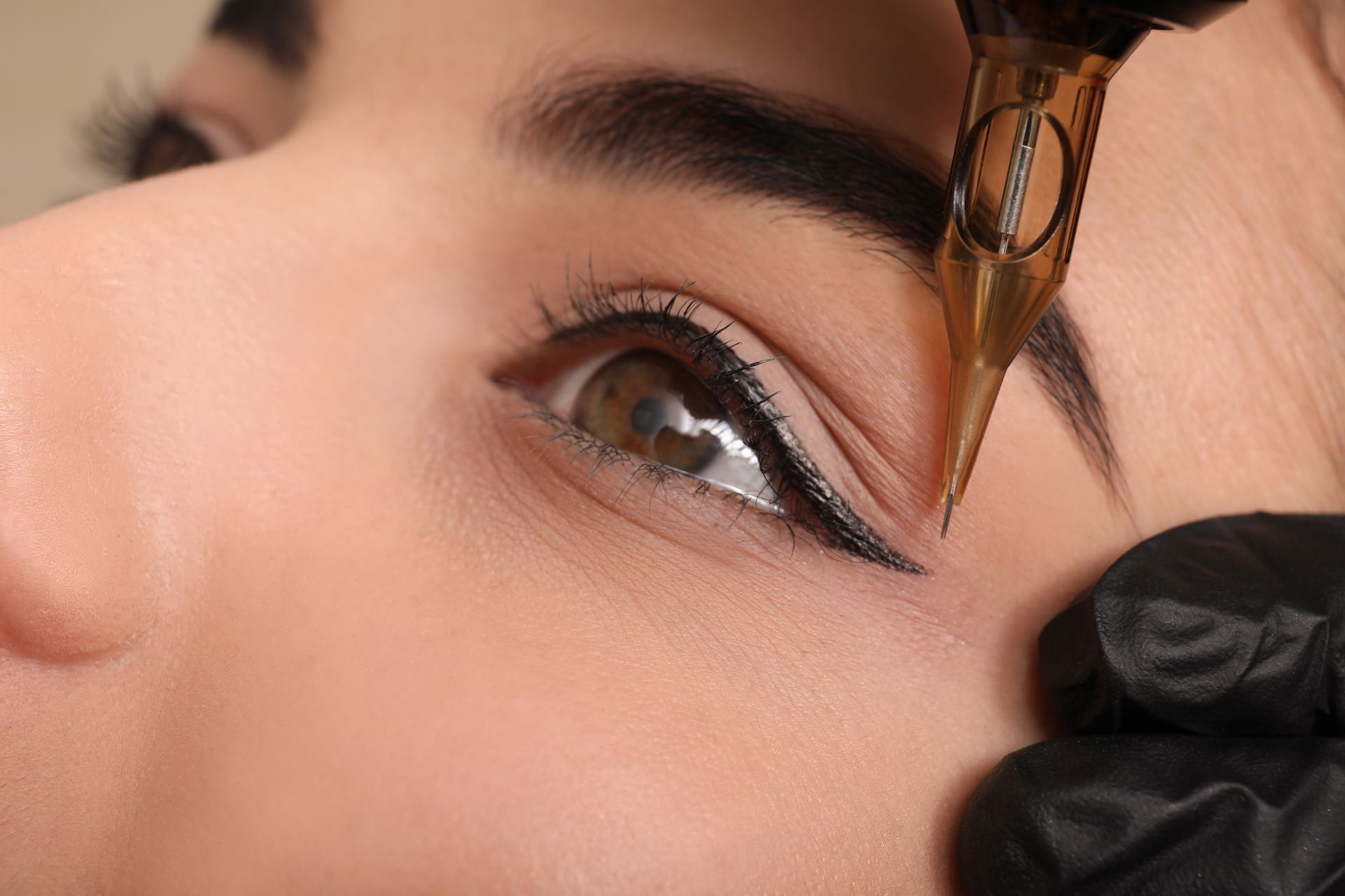 Eyeliner tattoo procedure in progress: black ink pen near eye, black gloves, light skin, close-up.