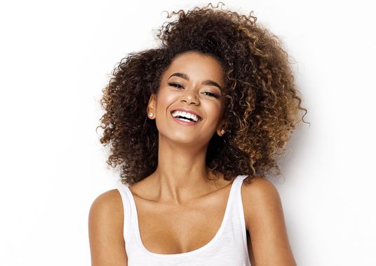 a woman with curly hair is smiling and wearing a white tank top .