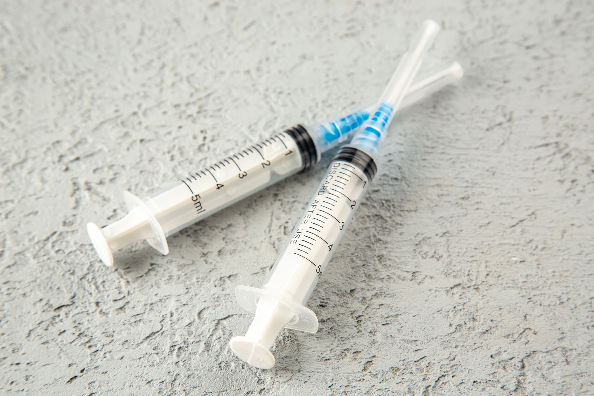Two syringes with clear liquid on a textured gray surface