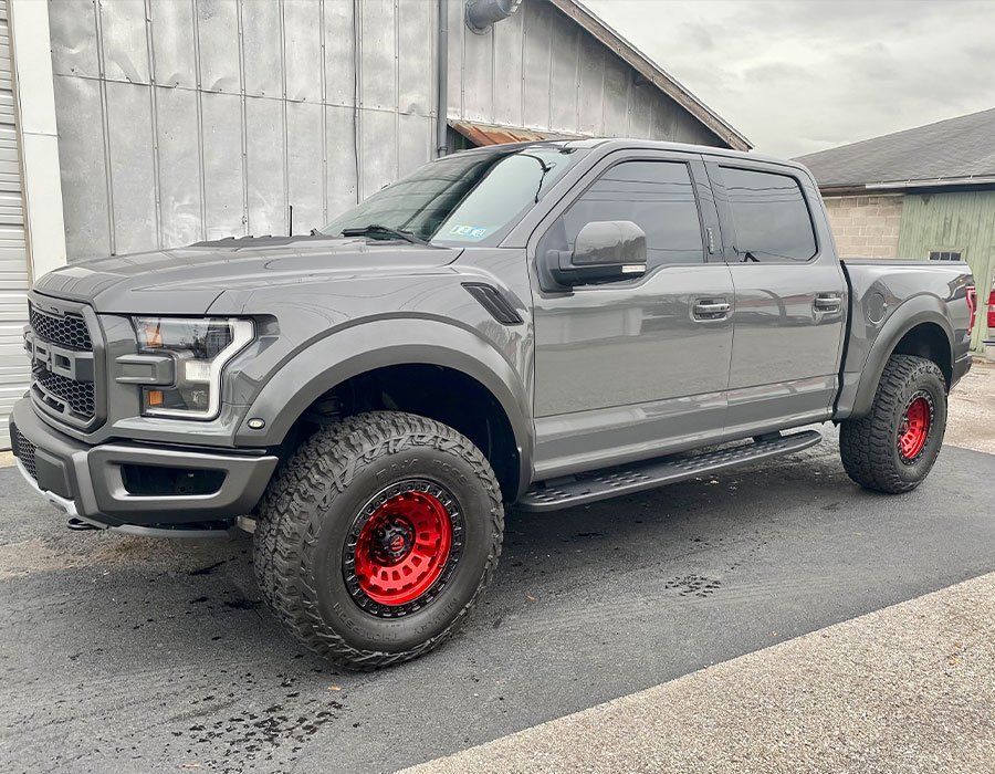 A gray ford raptor truck with red wheels is parked in front of a building.