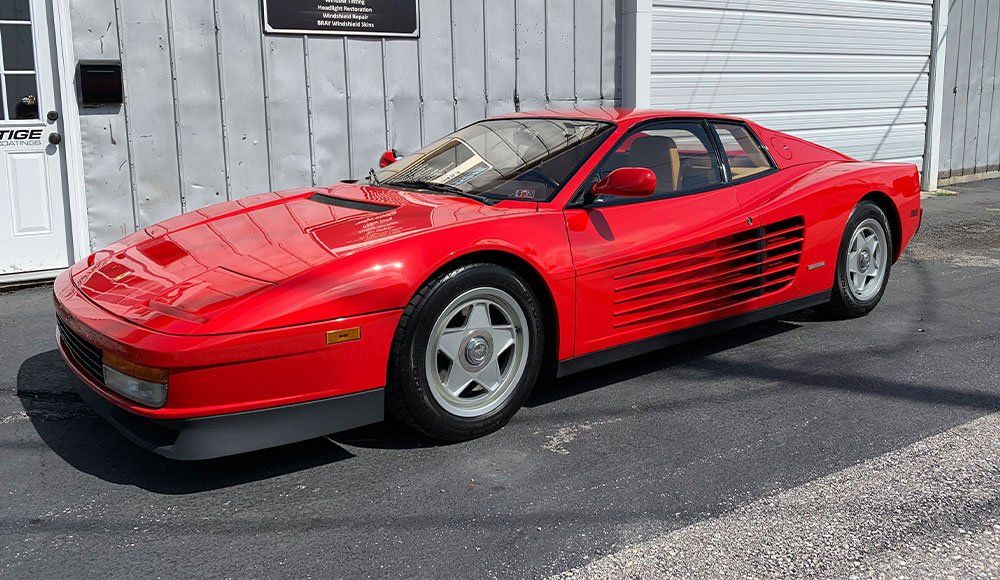 A red ferrari testarossa is parked in front of a garage.
