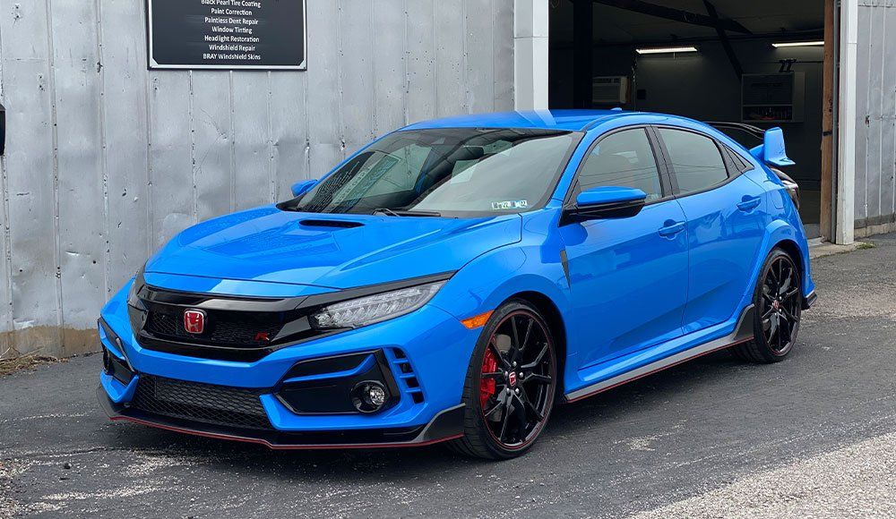 A blue honda civic type r is parked in front of a building.