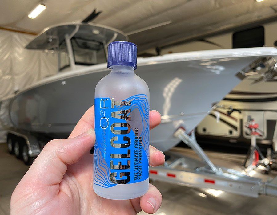 A person is holding a bottle of gelcoat in front of a boat.