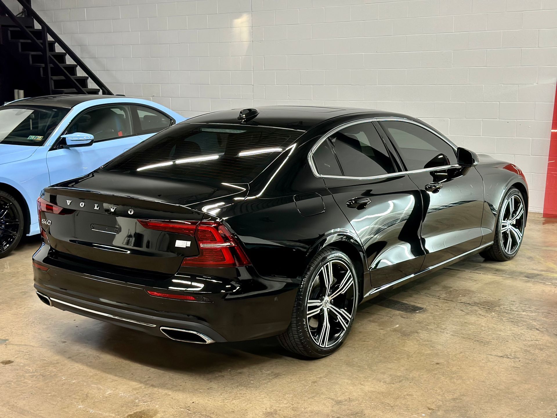 A black volvo s60 is parked in a garage next to a blue car.
