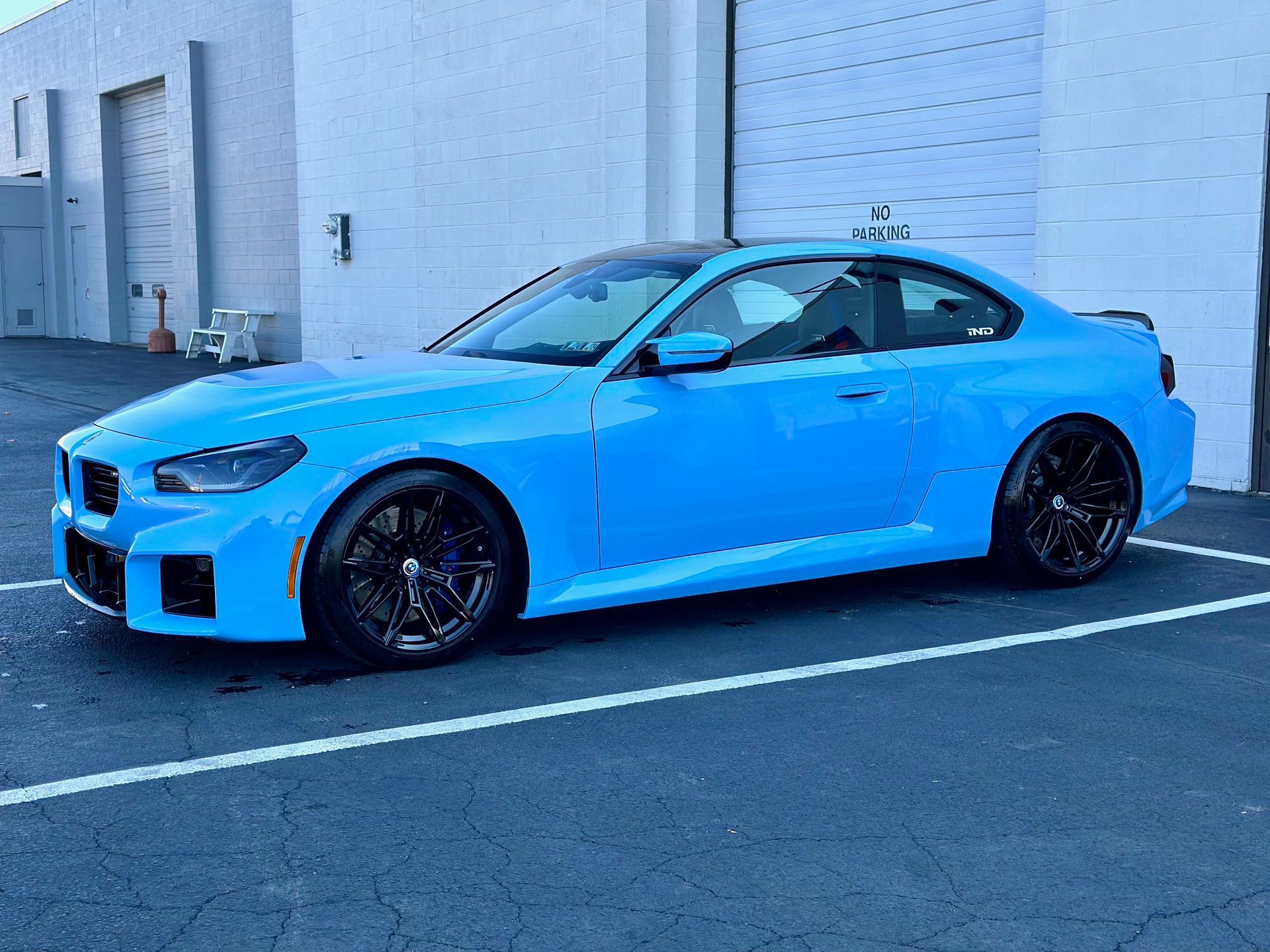 A blue bmw is parked in a parking lot in front of a building.