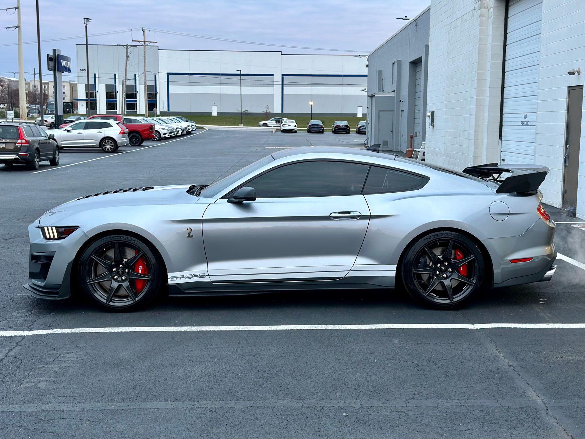 A silver mustang is parked in a parking lot in front of a building.