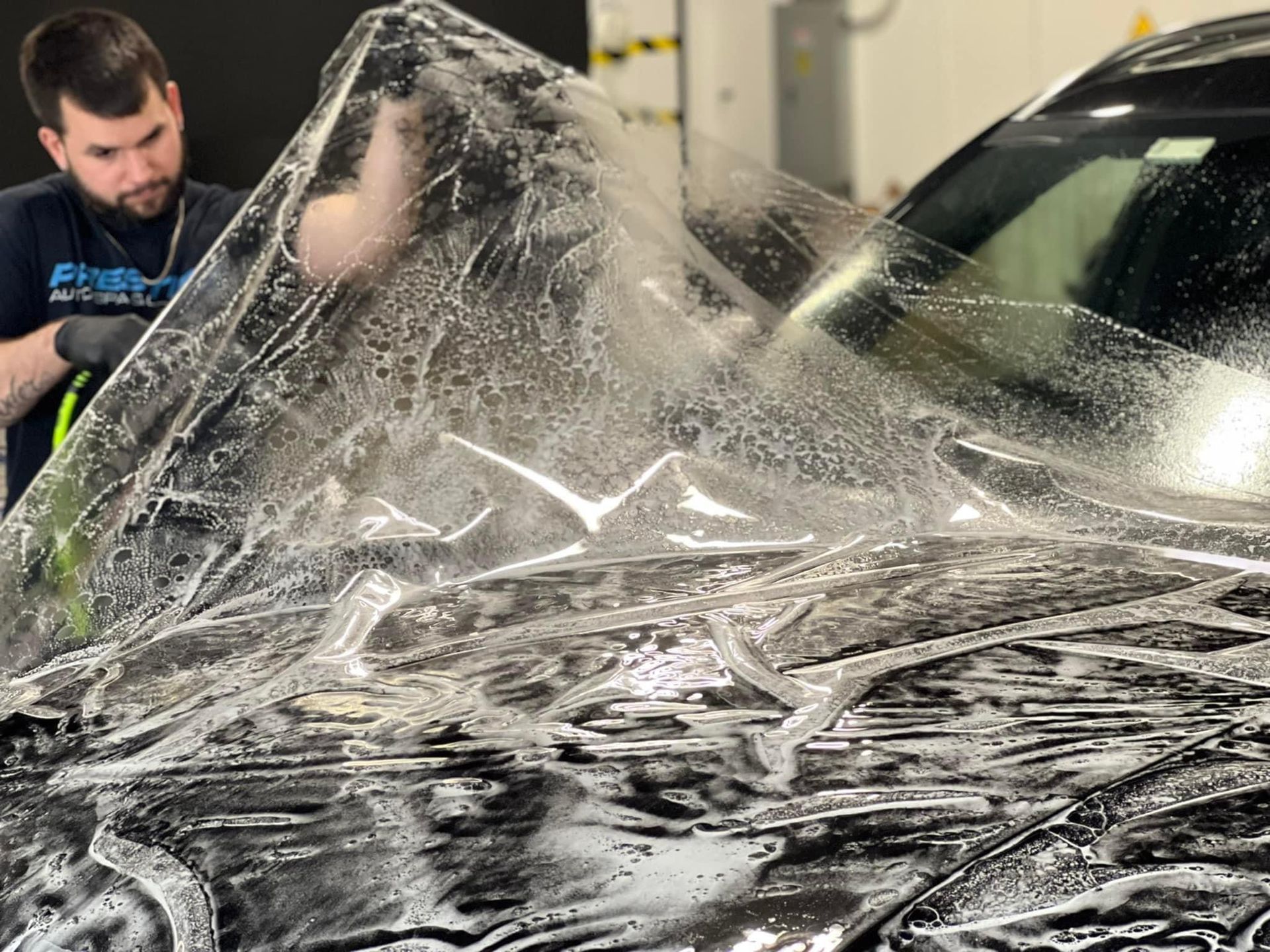 A man is covering a car with plastic wrap.
