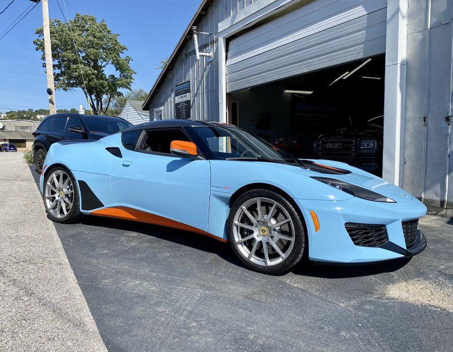 A blue and orange sports car is parked in front of a garage.