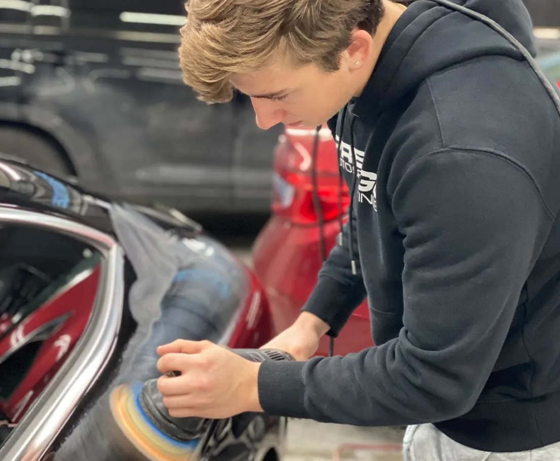 A man in a black hoodie is polishing a car