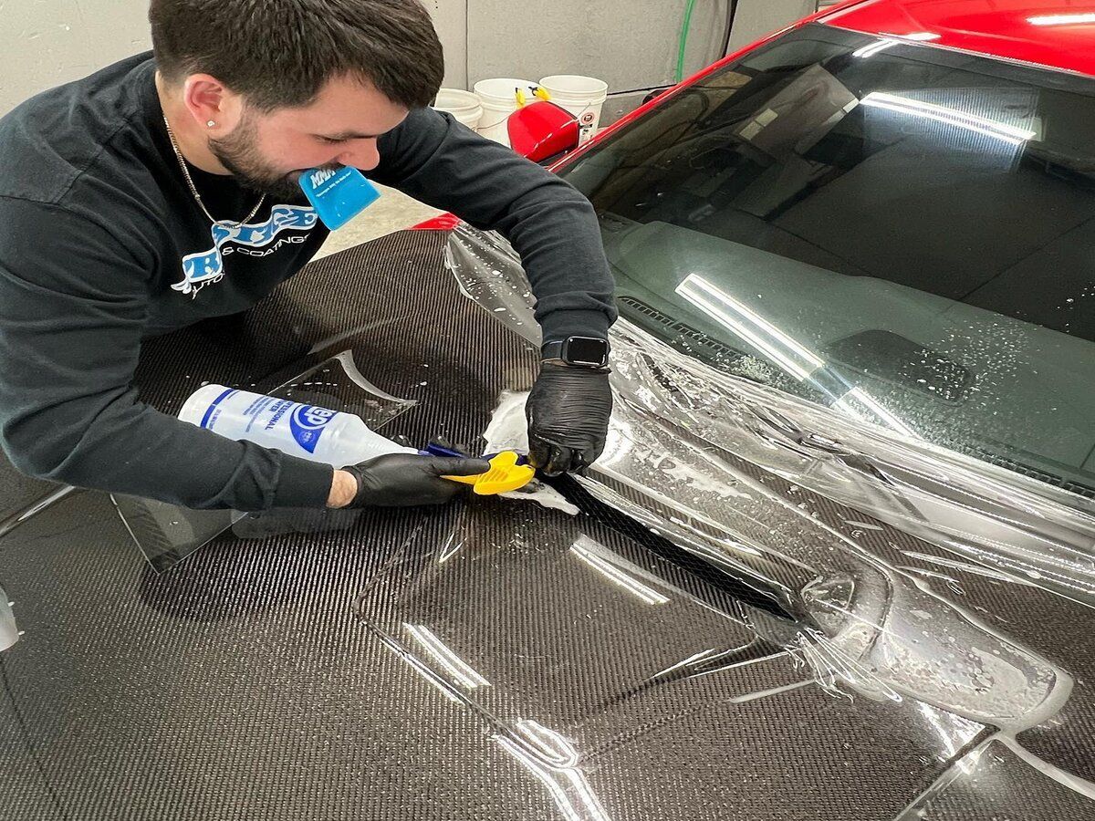 A man is covering the hood of a car with paint protection film