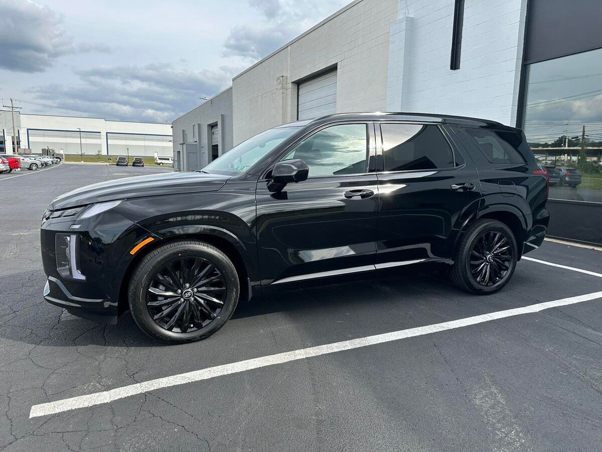 A black hyundai palisade is parked in a parking lot in front of a building.