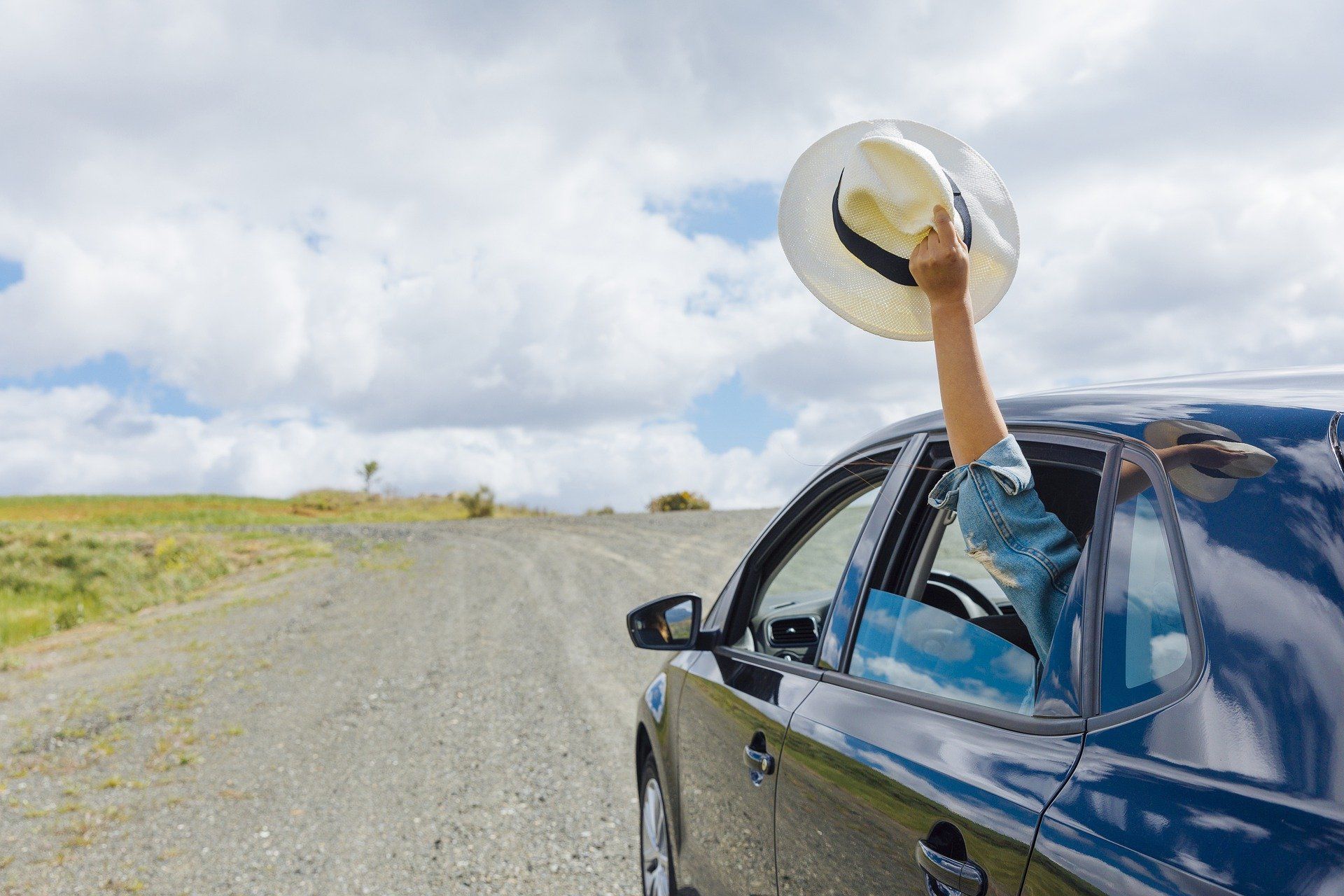 A person is holding a hat out of the window of a car.