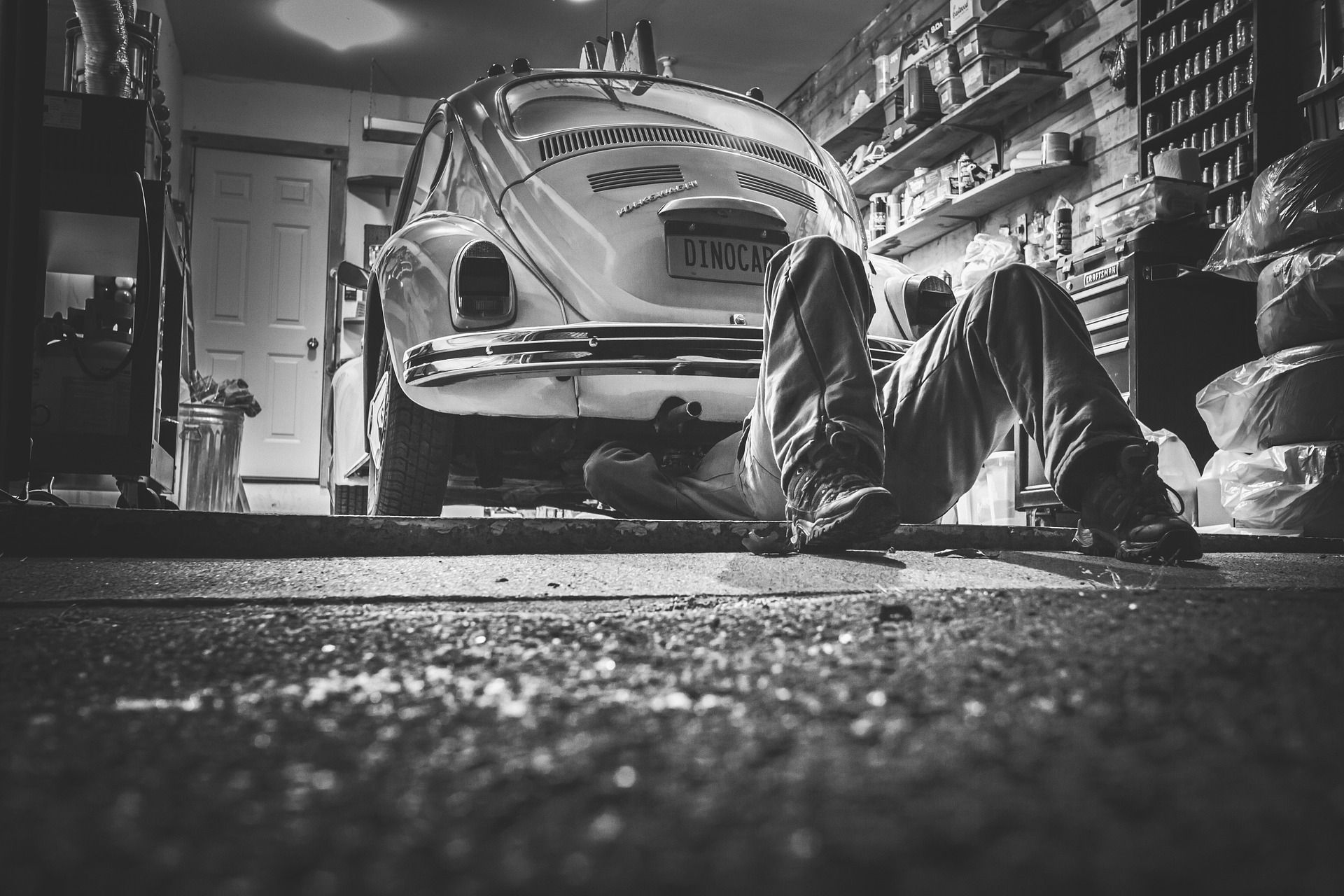 A man is laying on the ground working on a car in a garage.