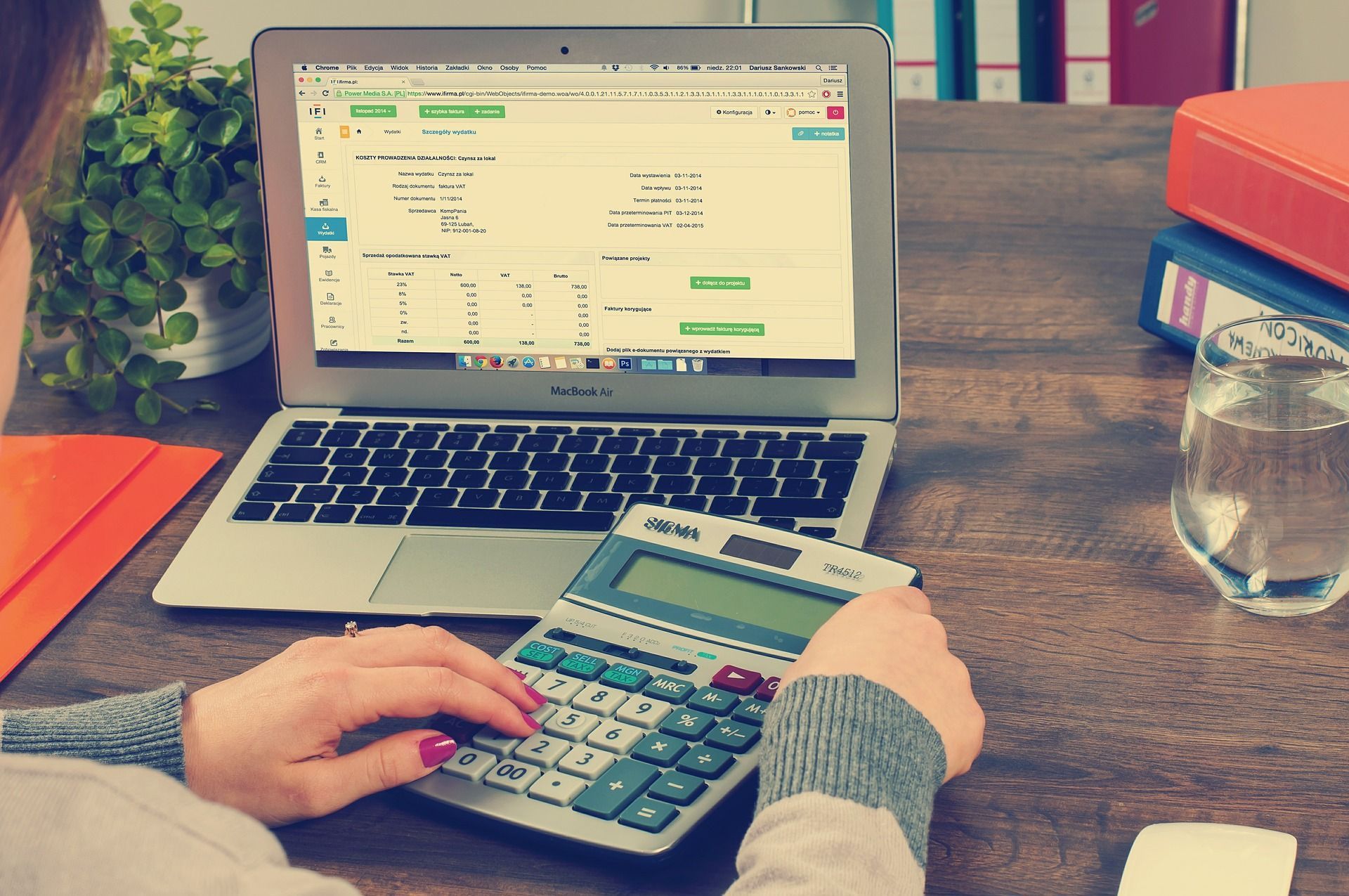 A woman is using a calculator in front of a laptop computer.