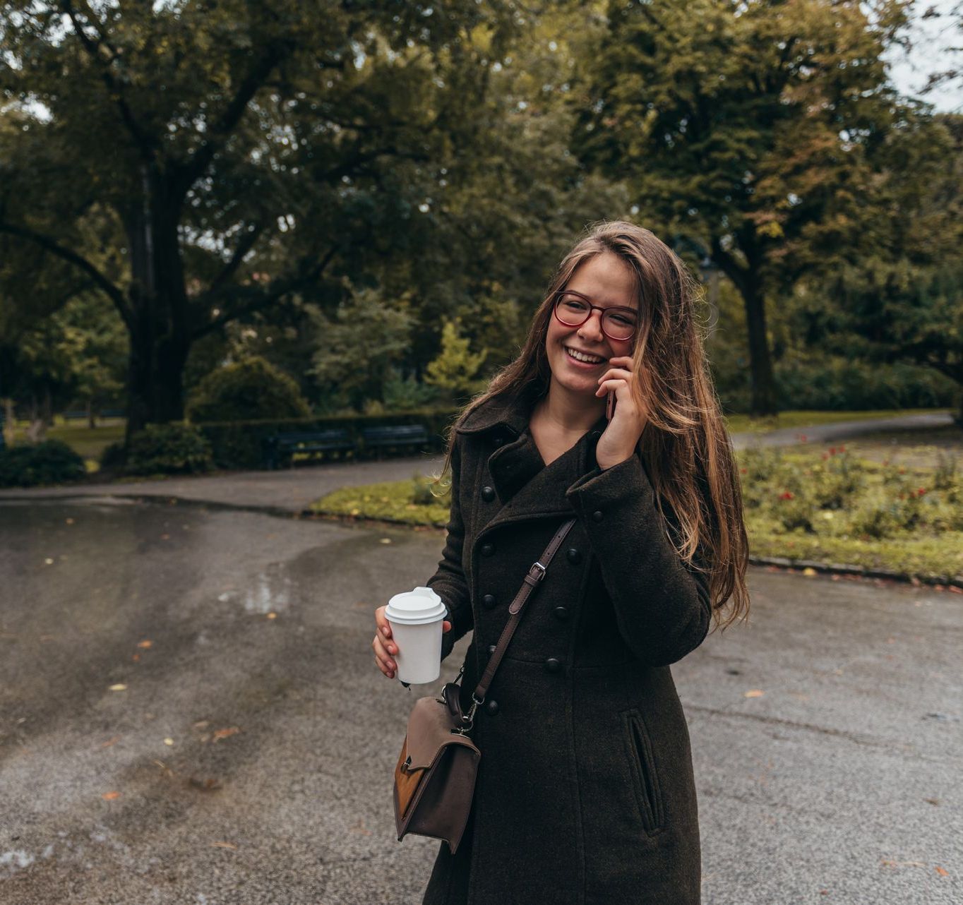 A woman is talking on a cell phone while holding a cup of coffee.