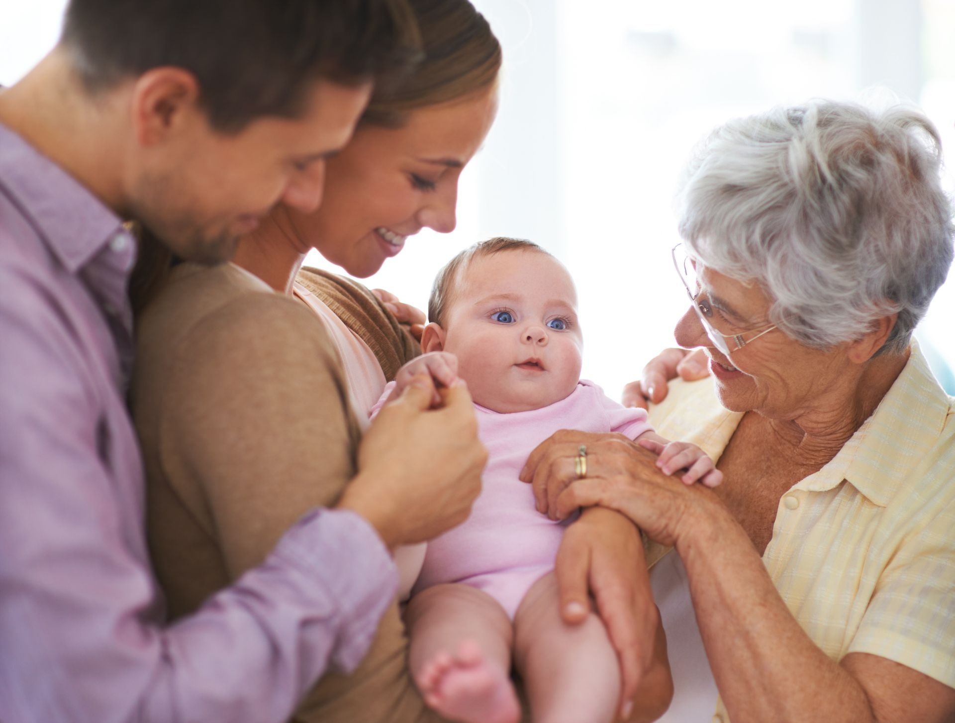 A family is holding a baby in their arms while an elderly woman looks on.