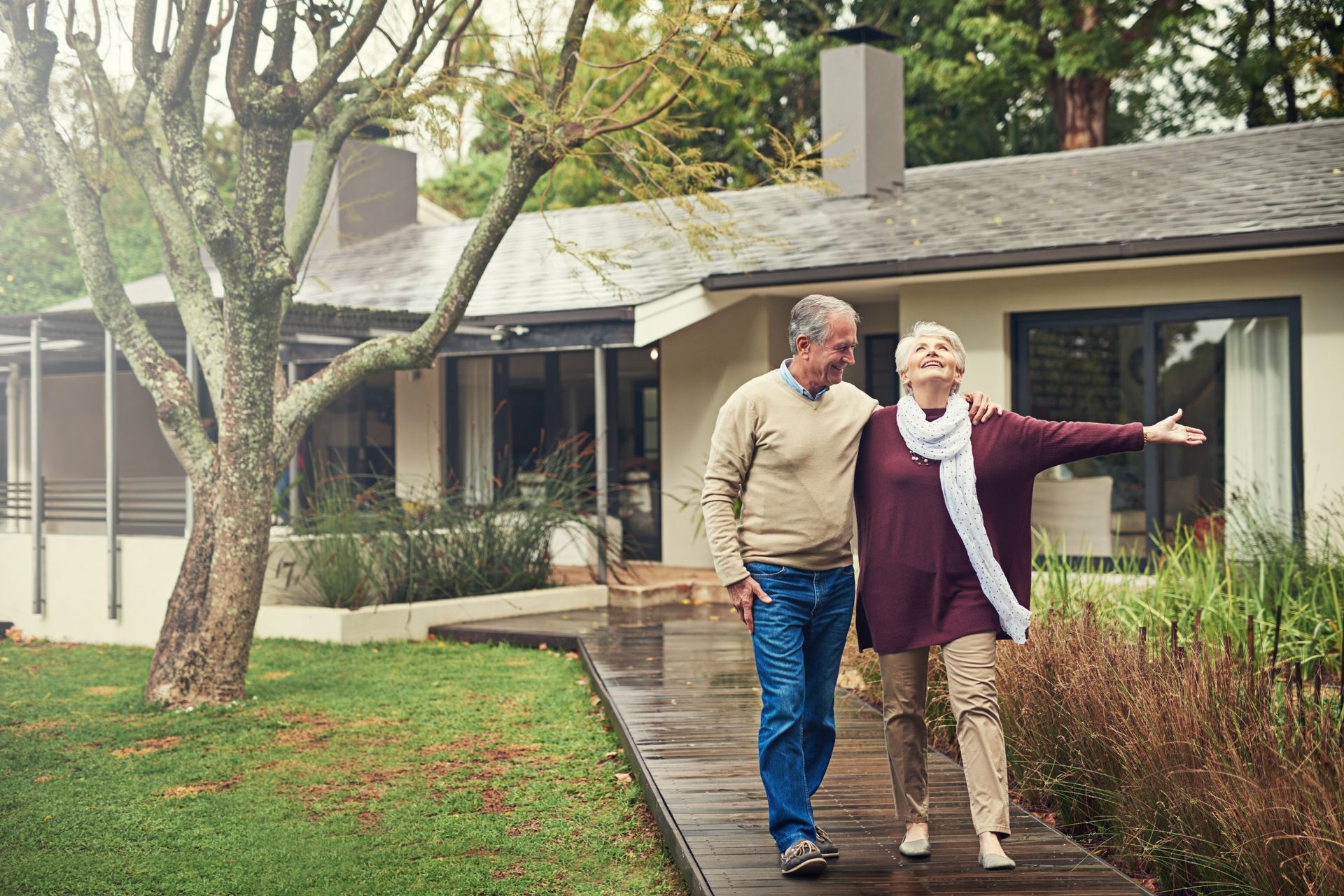 An elderly couple is walking down a path in front of their house.