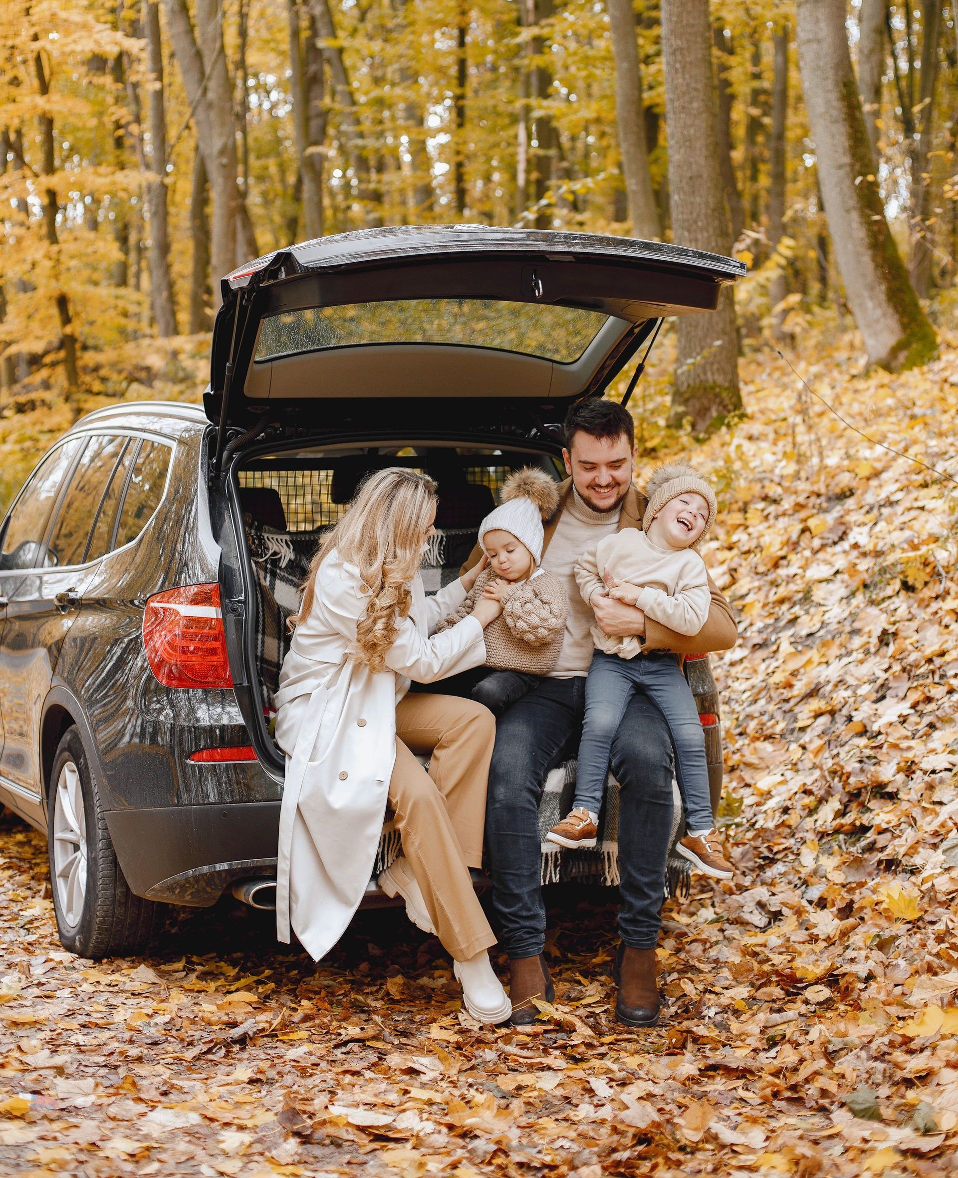 A family is sitting in the back of a car in the woods.