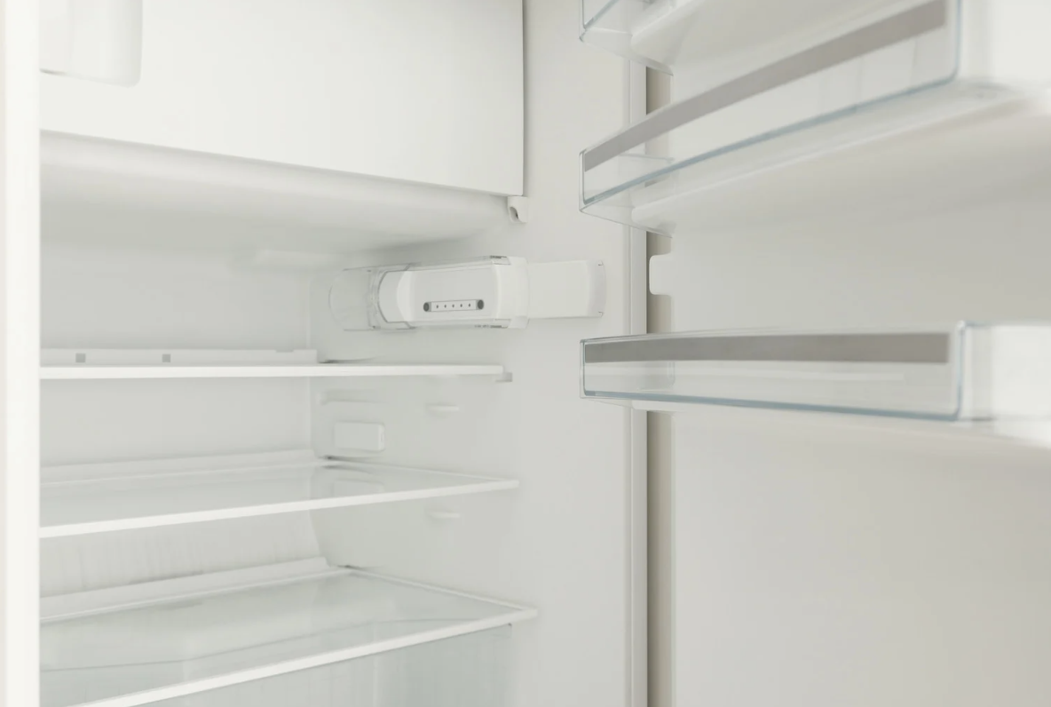 An empty refrigerator with the door open, shelves visible, white interior.