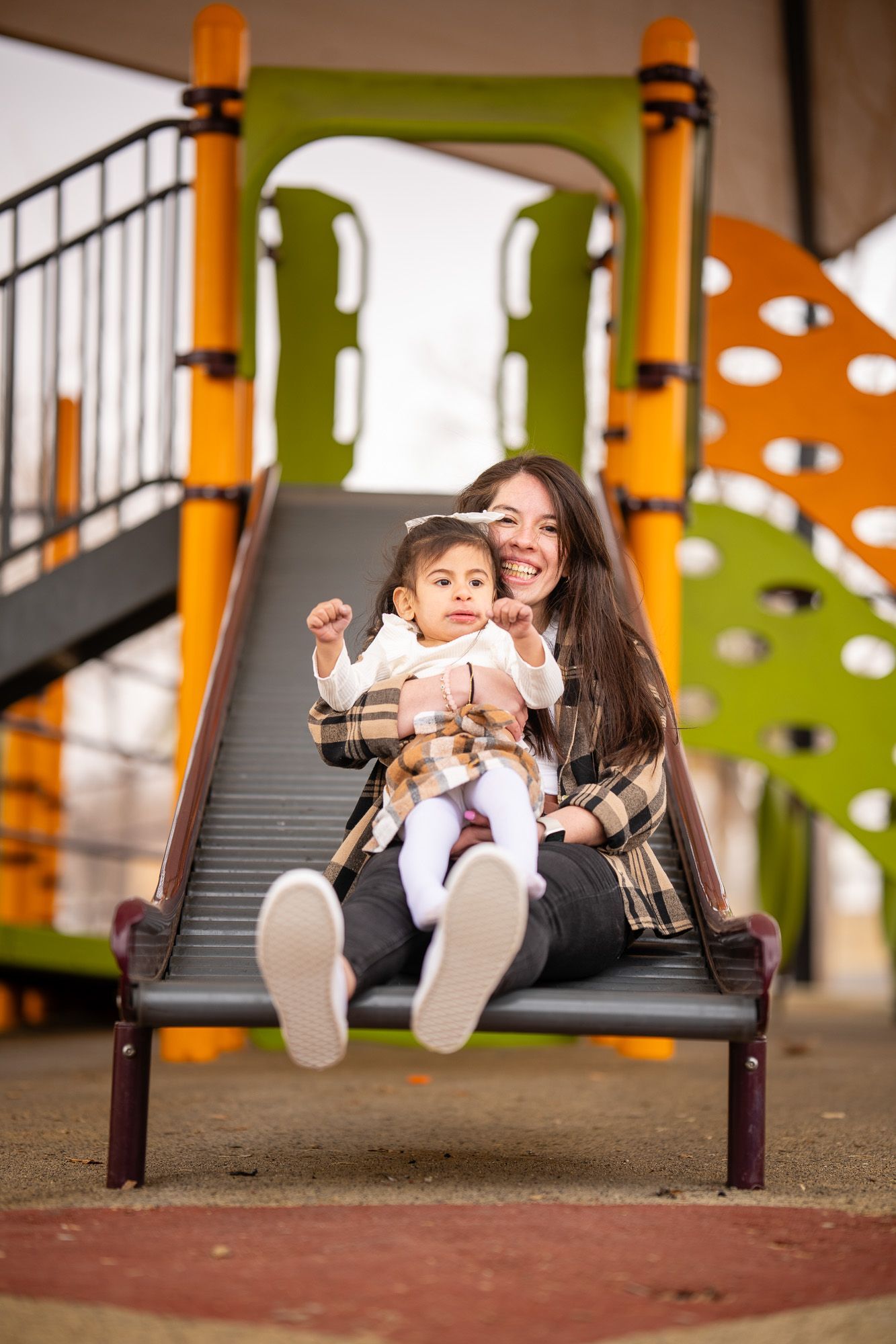 Mother and daughter smiling together while sliding at the playground, capturing the heart of Aprendamos Family of Services.