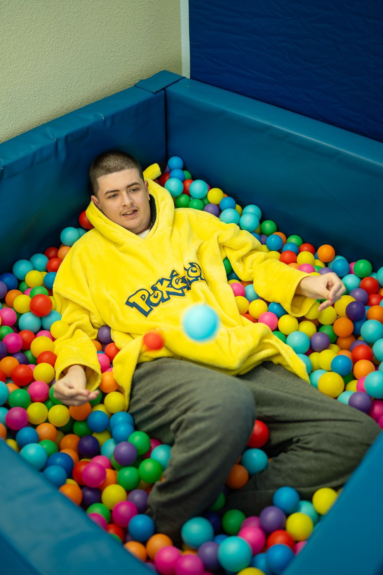 Teenage client at Mariposa Autism Service Center relaxing in a colorful ball pit during a sensory therapy session.