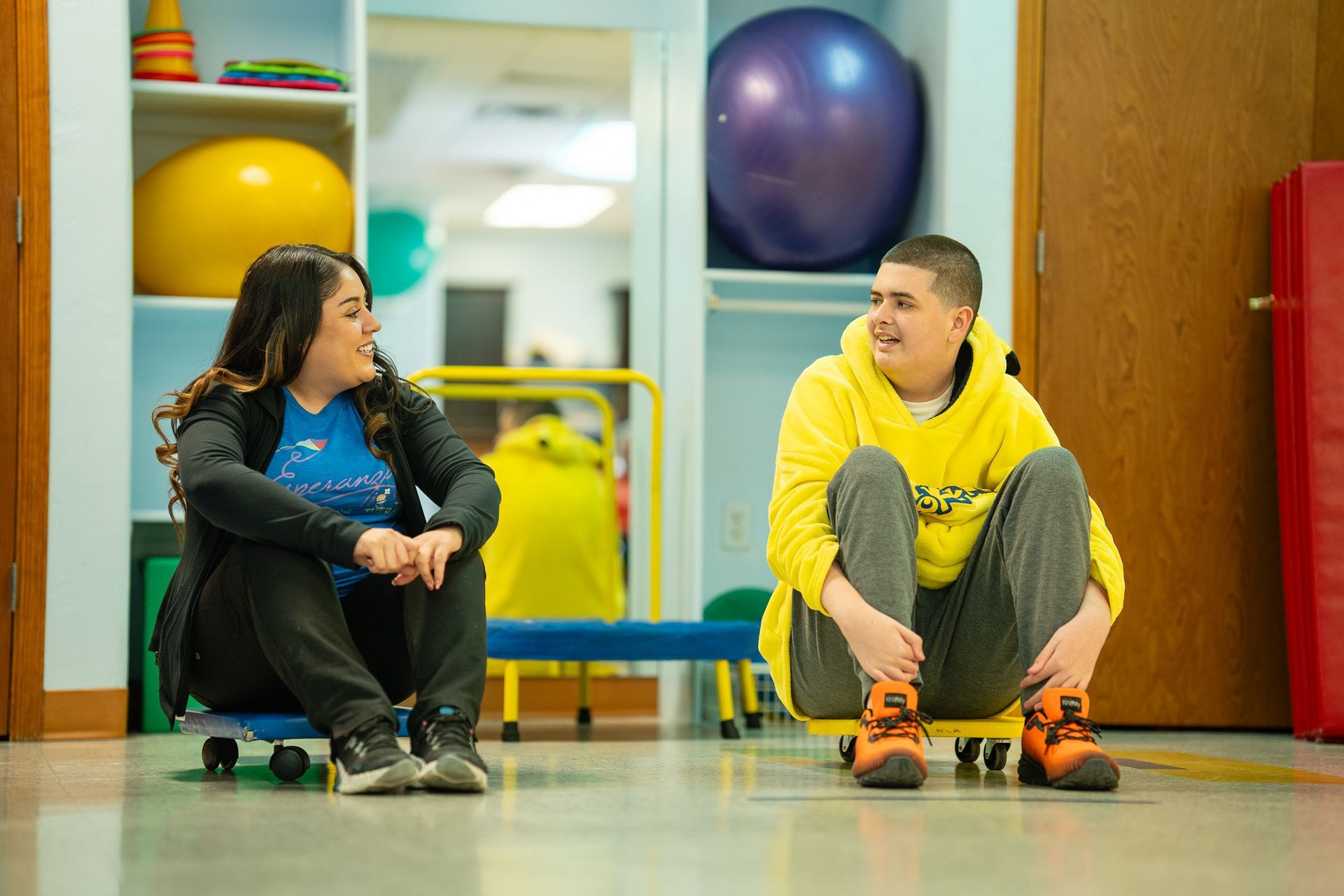 A kid and a therapist are sitting at a table looking at a tablet doing activities together.