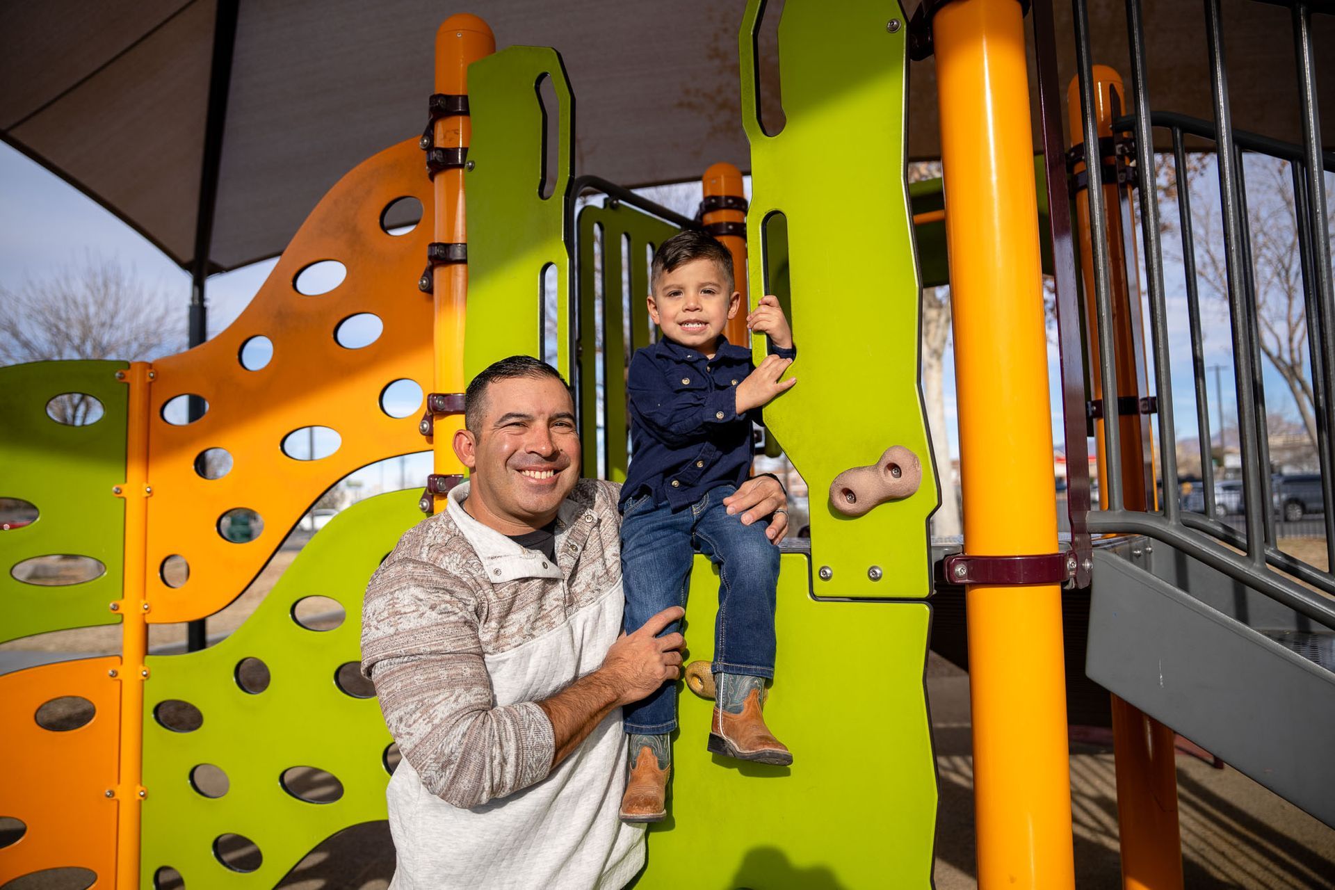 Smiling father holding his young son at a playground, representing the Conscious Fathering Program.