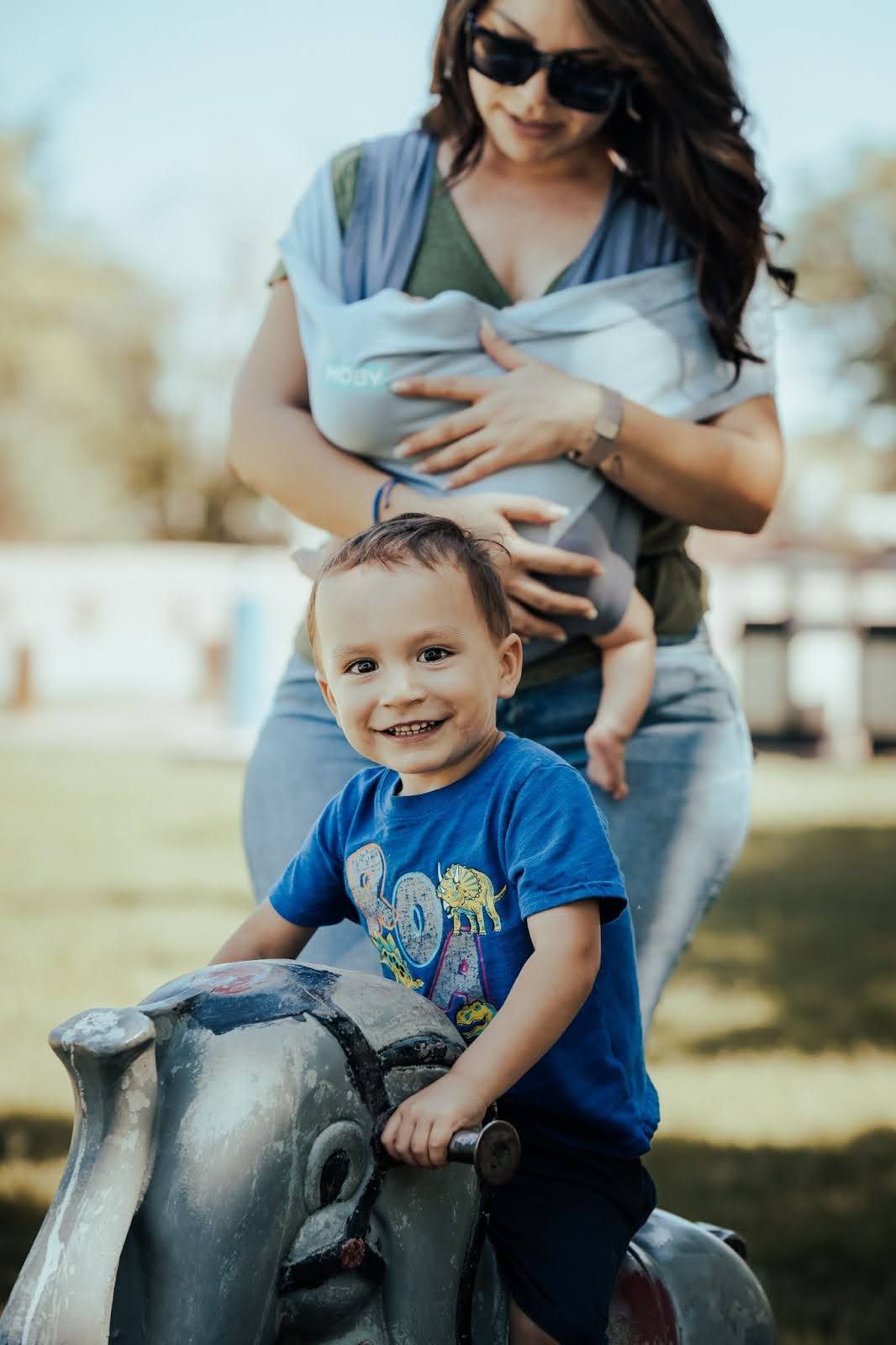 Smiling toddler in a blue shirt sitting on a park bench, with mom after receiving Aprendamos Early Intervention.