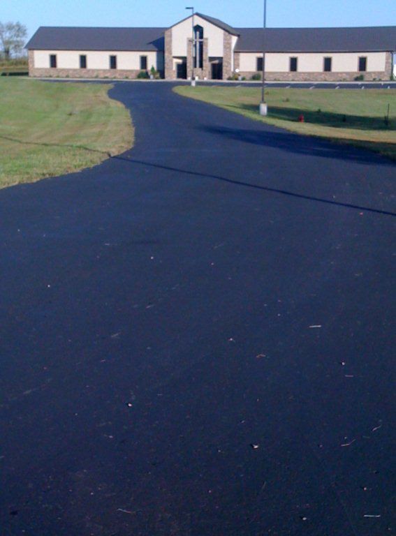 A driveway leading to a large building with a cross on it
