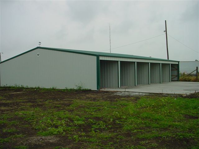 A white building with a green roof is sitting in the middle of a grassy field.