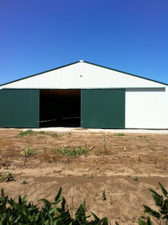 A white building with green sliding doors in a field