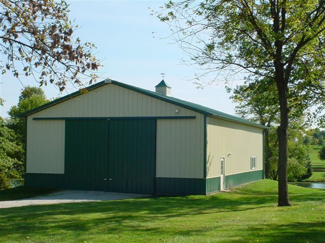 A white and green barn with a tree in front of it
