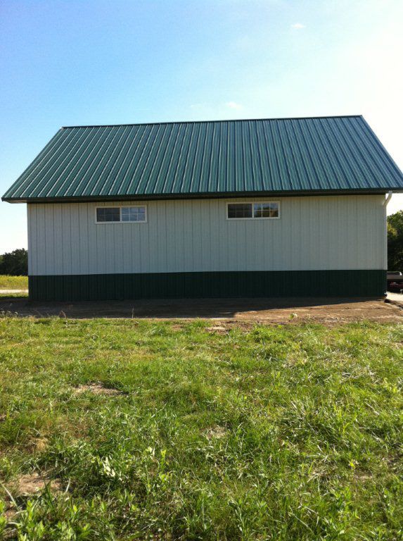 A white building with a green roof is sitting in the middle of a grassy field.