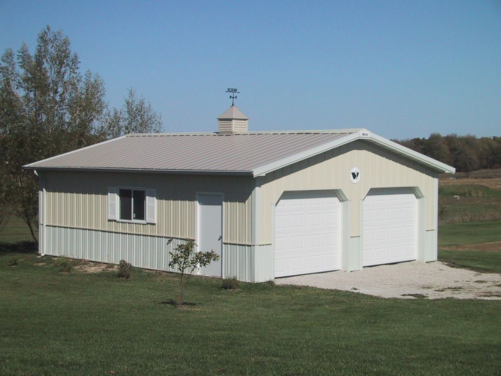 A garage with two garage doors is sitting in the middle of a grassy field