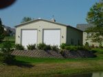 A garage with two garage doors is sitting on top of a grassy hill next to a pond.
