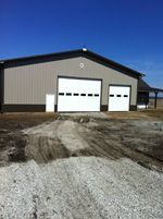 A large building with two garage doors is sitting on top of a dirt field.