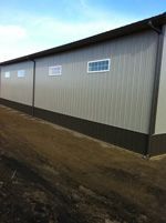 A large building with a lot of windows is sitting next to a dirt road.