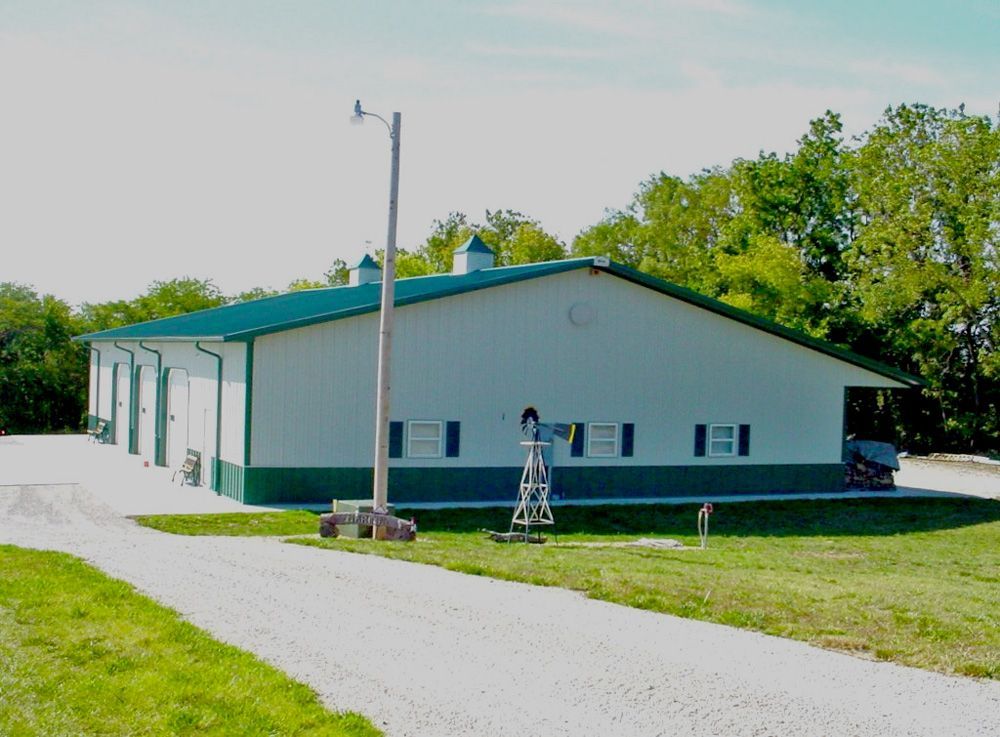 A large white building with a green roof sits in the middle of a grassy field