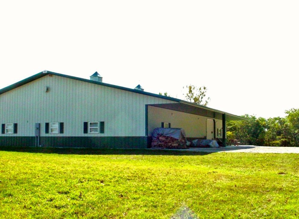 A large white and green building is sitting in the middle of a lush green field.