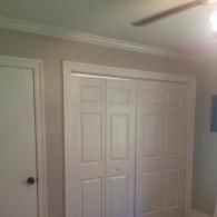 A beige bedroom wall featuring a white standard door on the left and a double white bifold closet door on the right.