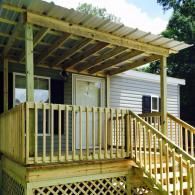 A wooden porch with a metal roof attached to a gray siding house, featuring stairs and lattice skirting.