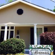 Tan house with a front porch, white columns, and a sign in front that reads 