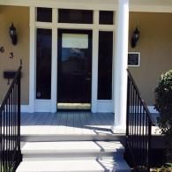 A front porch with white steps, a black door with glass panels, black railings, and two wall-mounted lanterns.