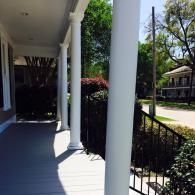 A covered porch with white columns overlooking a residential street on a sunny day.