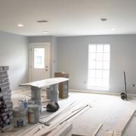 A room under renovation with light gray walls, a window, a white door, a temporary table, and construction supplies.