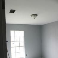 A view of a room with gray walls, a white ceiling with a light fixture and square vent, and a window with white grids.