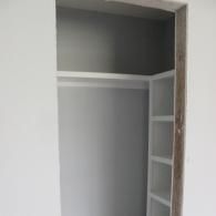 An open closet with white walls and shelving, featuring a built-in vertical storage unit on the right side.