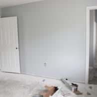 A light gray wall in a room under renovation, featuring a white door, a wall outlet, and construction debris on the floor.